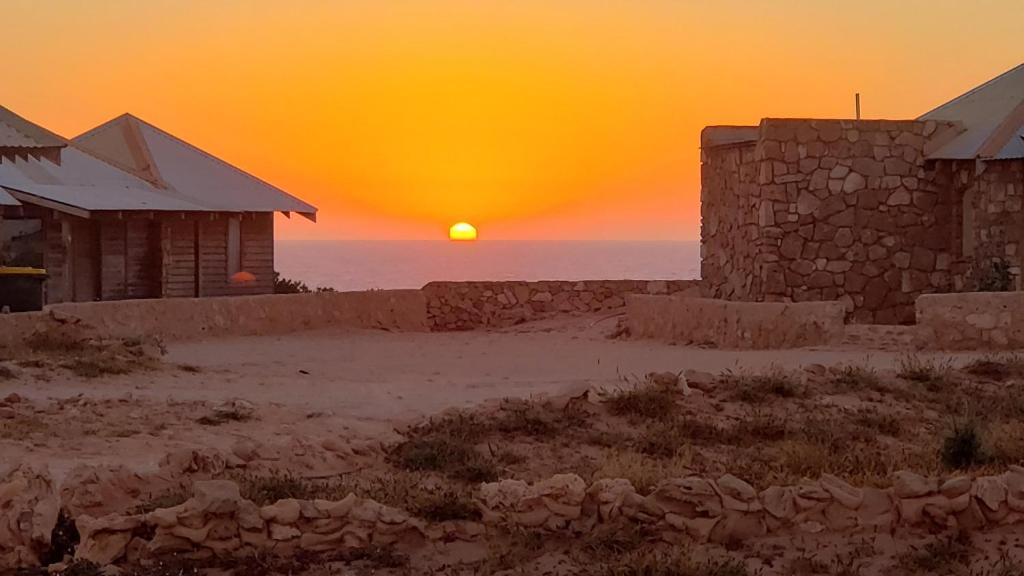 einen Sonnenuntergang über dem Meer mit zwei Steingebäuden in der Unterkunft Gnaraloo Station - Homestead in Carnarvon