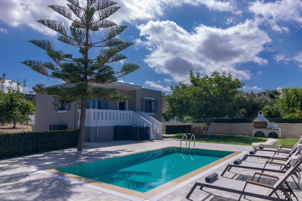 a pool with chairs and a tree next to a house at Villa Sofia in Áyios Konstandínos