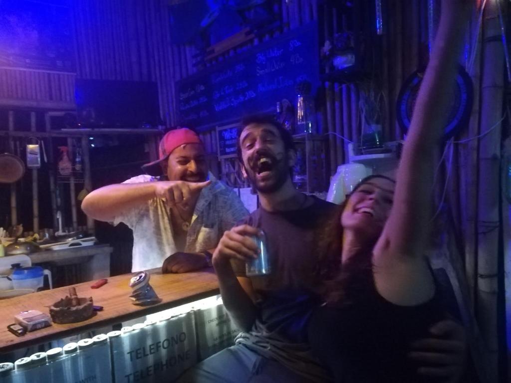 tres personas sentadas en un bar con los brazos en el aire en Perezoso Hostel, en Rurrenabaque