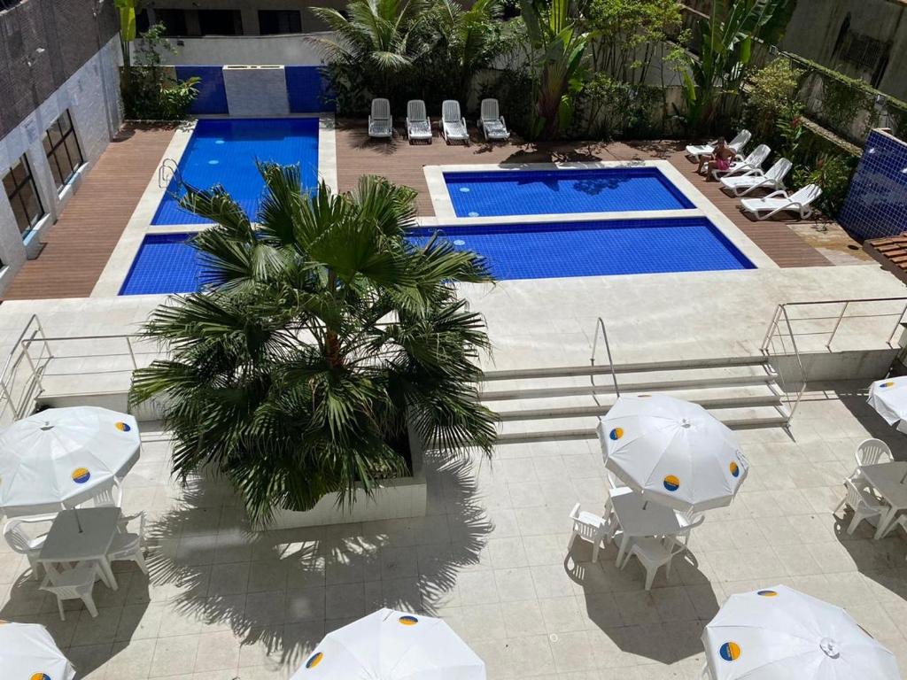 een zwembad met witte parasols en stoelen en een palmboom bij Flat top Guarujá in Guarujá