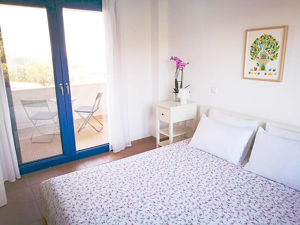 a white bedroom with a bed and a balcony at Olive Bay Hilltop Apartments Ammouliani in Ammouliani