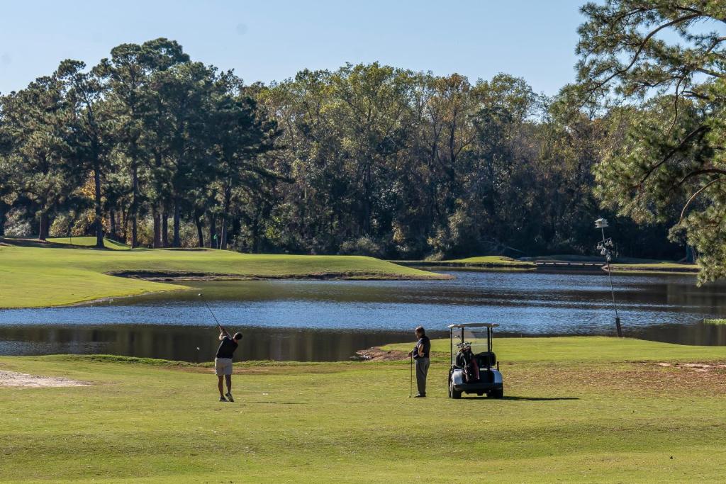 zwei Leute spielen Golf neben einem See in der Unterkunft Dothan National Golf Club and Hotel in Dothan