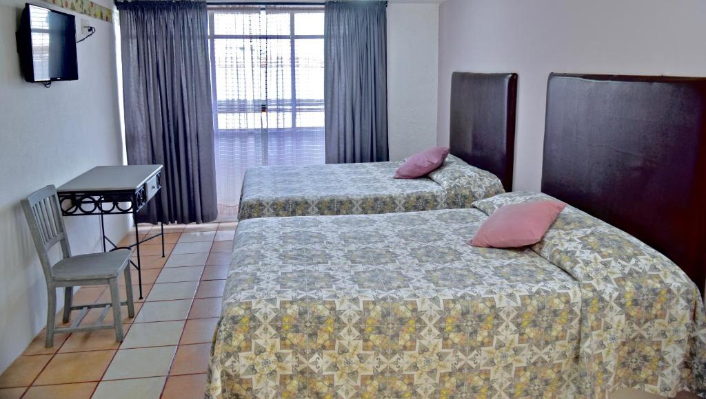 een hotelkamer met 2 bedden, een bureau en een raam bij Hotel Posada Centenario in Ixmiquilpan