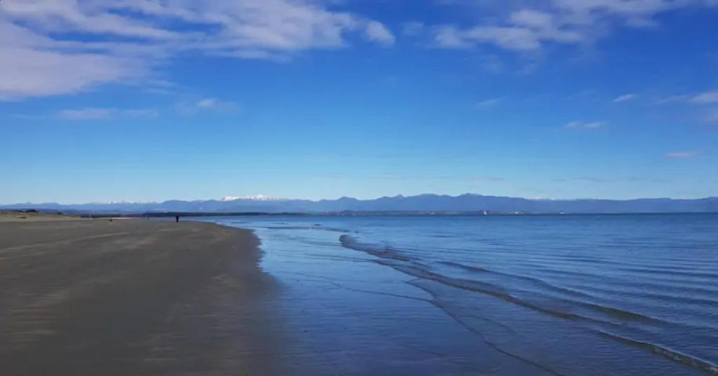 a beach with water and a blue sky and clouds at Studio on Parkers in Nelson
