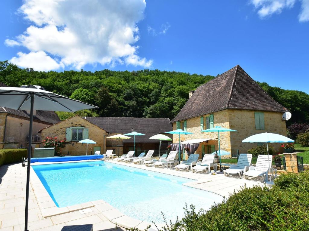 a swimming pool with chairs and umbrellas next to a building at Stone house with shared pool near Sarlat in Prats-de-Carlux