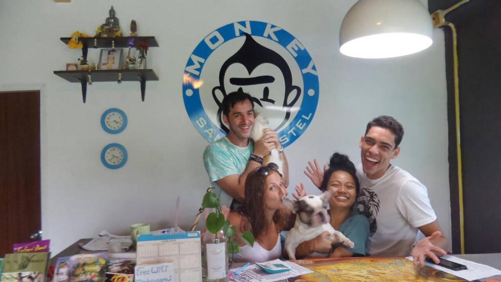 un grupo de personas sentadas en una mesa con un perro en Monkey Samui Hostel, en Choeng Mon Beach