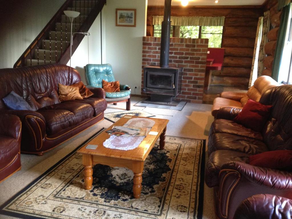 a living room with leather couches and a fireplace at Canobolas Mountain Cabins in Lidster