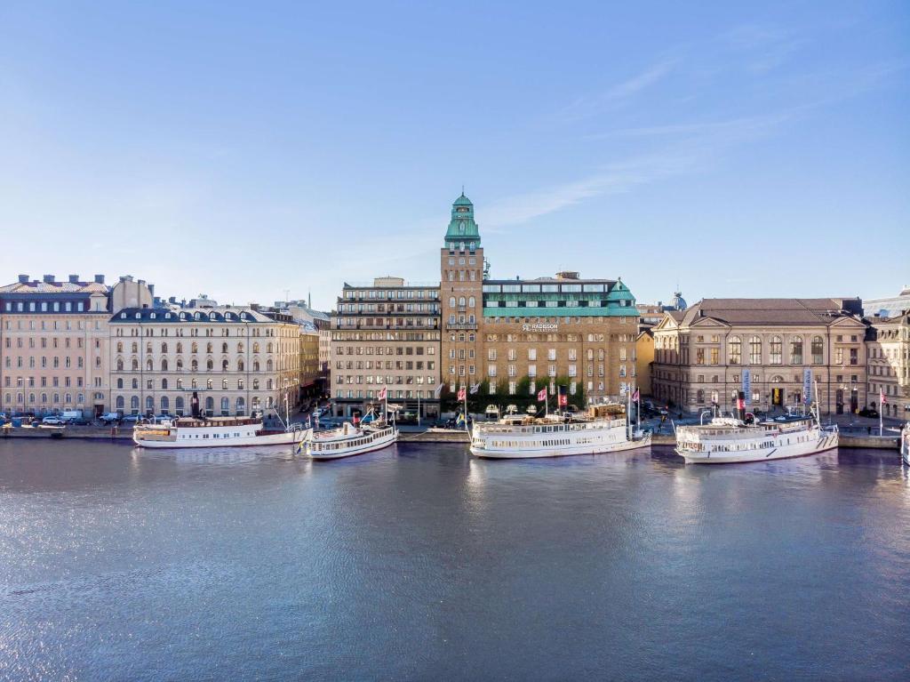 un groupe de bateaux amarrés dans une rivière avec des bâtiments dans l'établissement Radisson Collection, Strand Hotel, Stockholm, à Stockholm