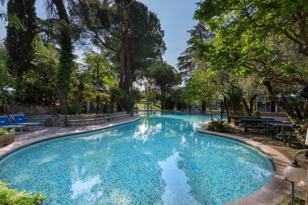 a swimming pool in a park with trees at Hotel Marco Polo in Garda