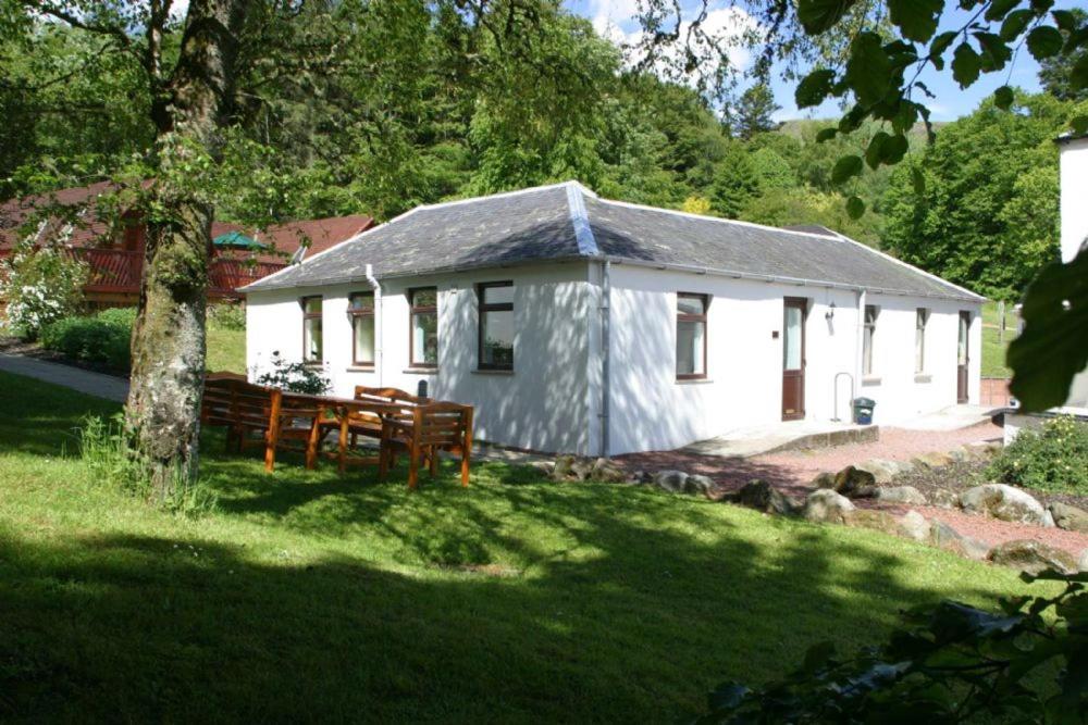 una pequeña casa blanca con un banco en un patio en Doonans Cottage, en Maybole