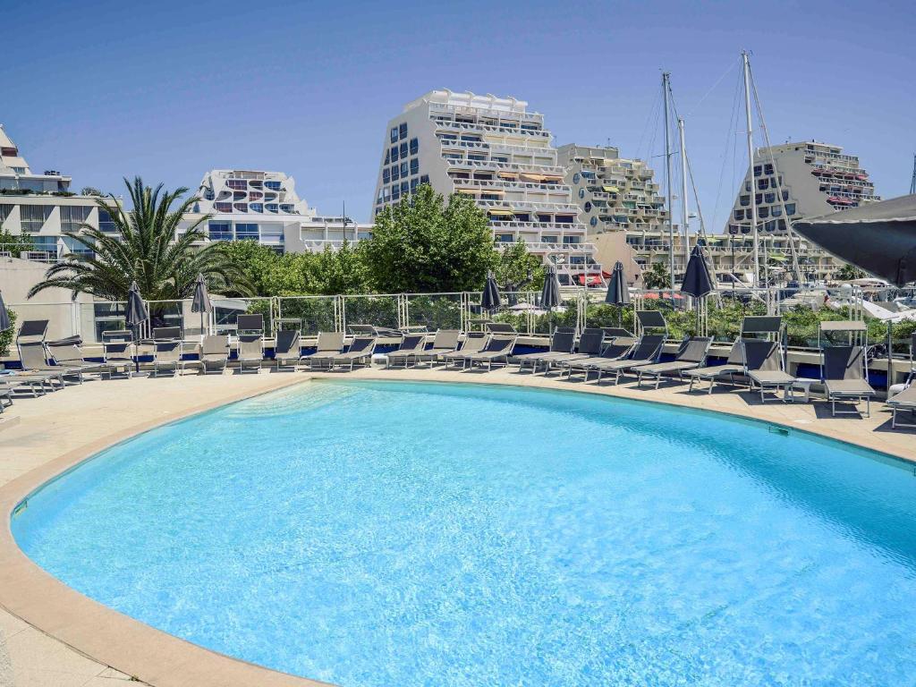 a large swimming pool with lounge chairs and buildings at Mercure Port La Grande Motte in La Grande Motte
