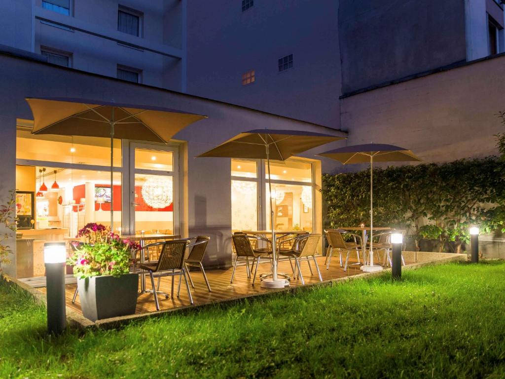 un patio con mesas, sillas y sombrillas por la noche en ibis Paris Vanves Parc des Expositions, en Vanves