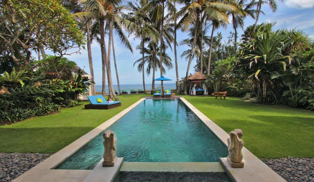 a swimming pool in a yard with palm trees at Villa Samudra Luxury Beachfront in Ketewel