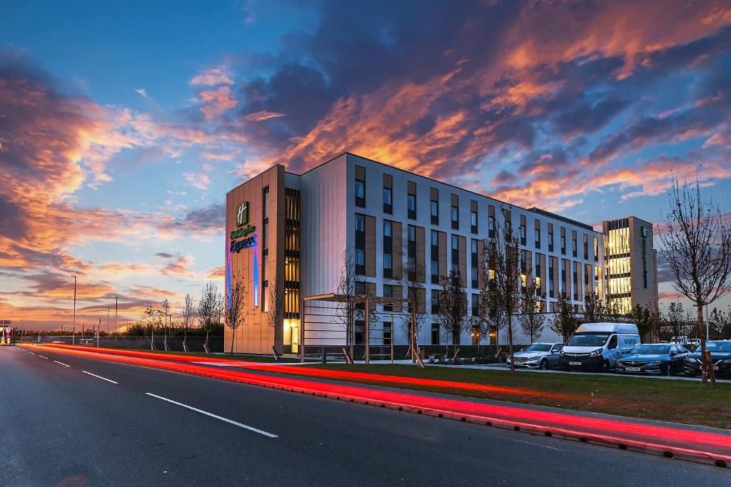 Holiday Inn Express - Bicester, an IHG Hotel في بيسستر: مبنى على جانب طريق مع غروب الشمس