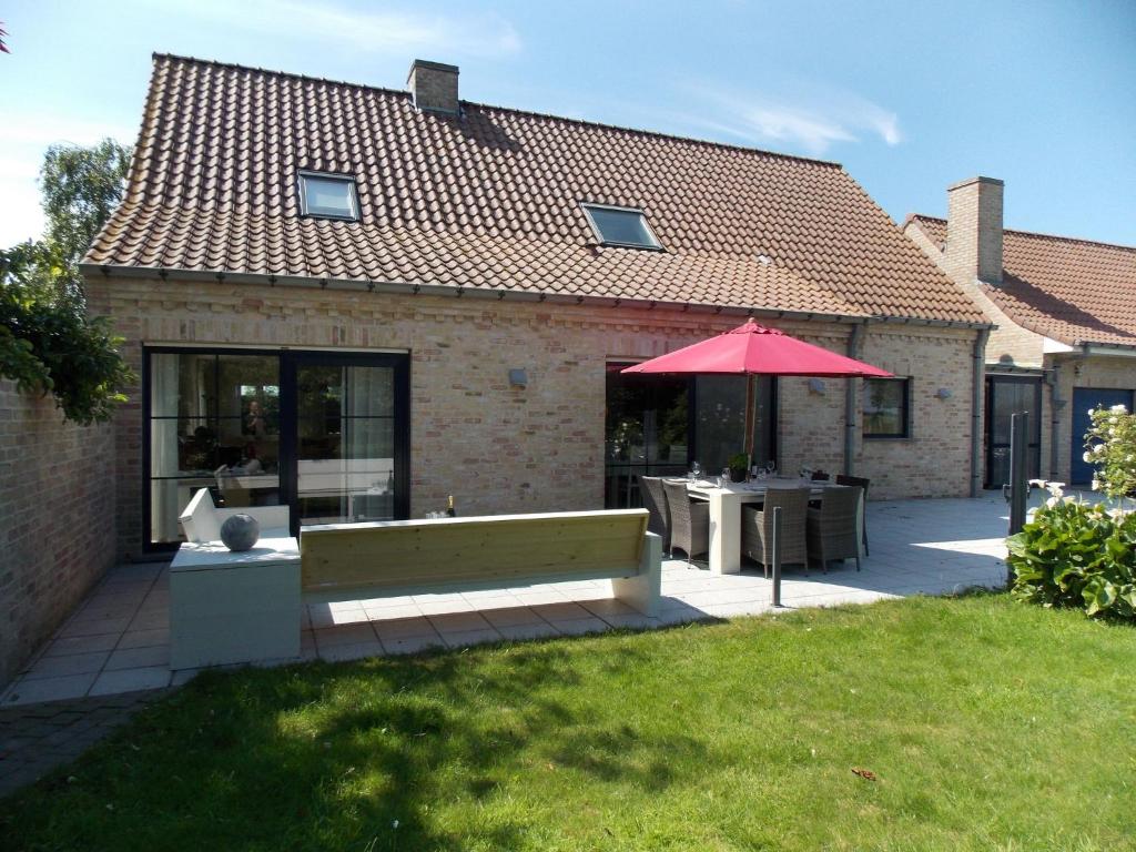 ディクスムイデにあるSun kissed Villa in Diksmuide with Garden Saunaの庭にベンチと傘を持つ建物