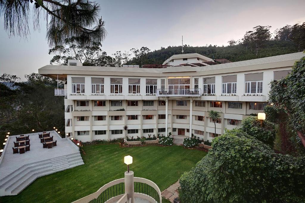 un gran edificio blanco con césped delante en Sinclairs Retreat Ooty, en Ooty