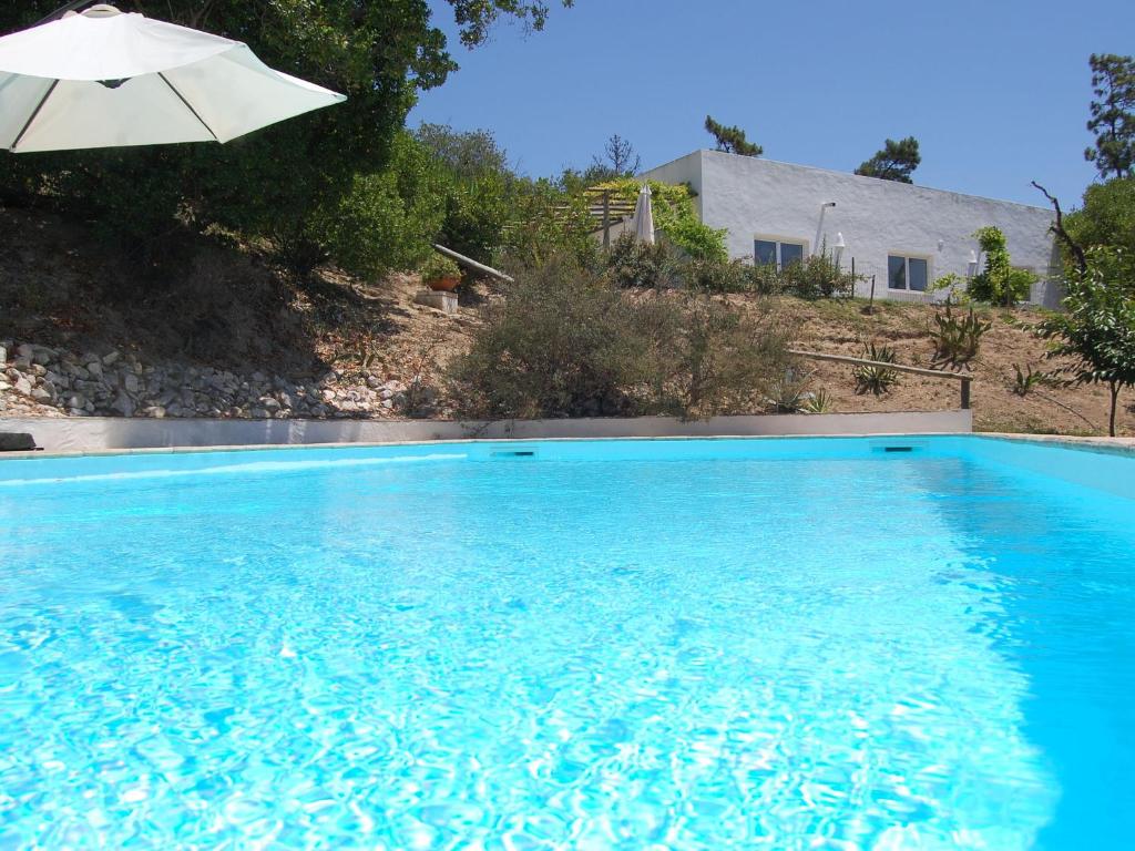 ein blauer Pool mit Sonnenschirm und ein Haus in der Unterkunft A Perfect villa with pool terrace and garden in Alcobaça