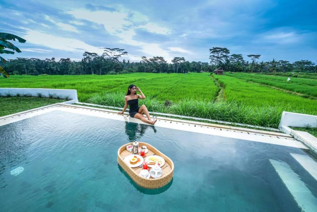 une femme assise dans une piscine avec un bateau dans l'eau dans l'établissement 2 BR Villa with open view of rice paddies & sunset, à Gianyar