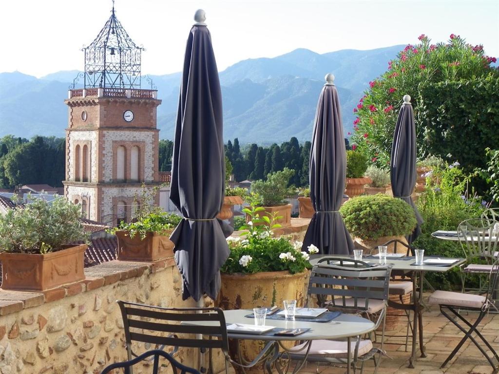 un patio con mesas, sombrillas y una torre de reloj en Château d'Ortaffa, en Ortaffa