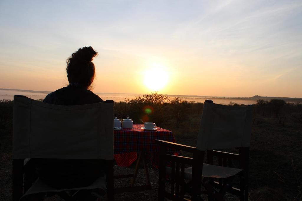 Una donna seduta a un tavolo a guardare il tramonto di Osero Serengeti Luxury Tented Camp a Banagi