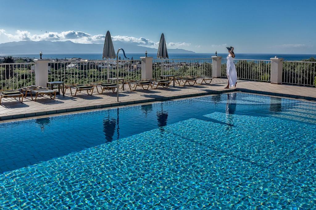 a woman is standing next to a swimming pool at Cretan Blu Platanias in Plataniás