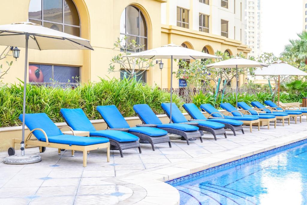 a row of blue chairs and umbrellas next to a pool at Royal Beach Residence in Dubai