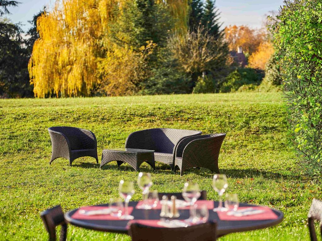 three chairs and a table with wine glasses on it at Novotel Senart Golf De Greenparc in Saint-Pierre-du-Perray