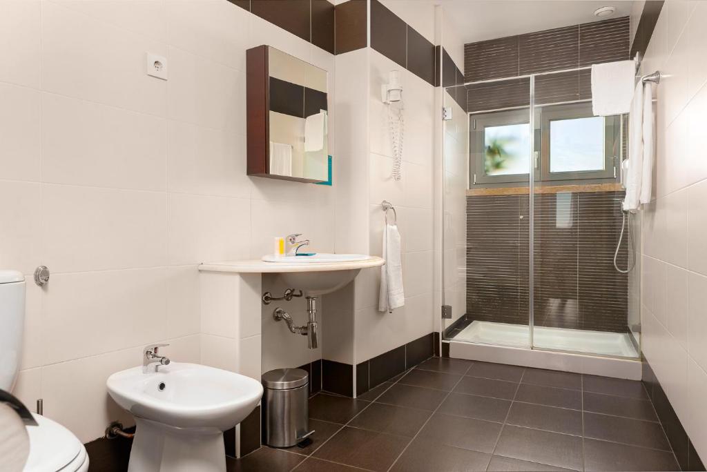 A tiled bathroom with a pedestal toilet, compact basin and glass-enclosed shower.