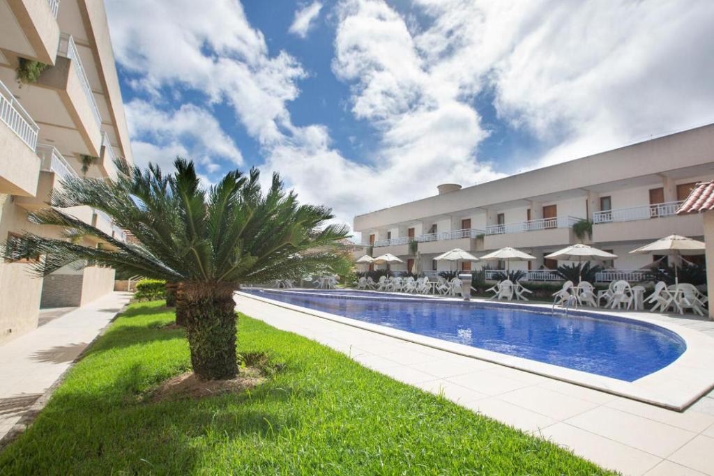 a palm tree in front of a building with a swimming pool at Porto da Serra Hotel in Gravatá