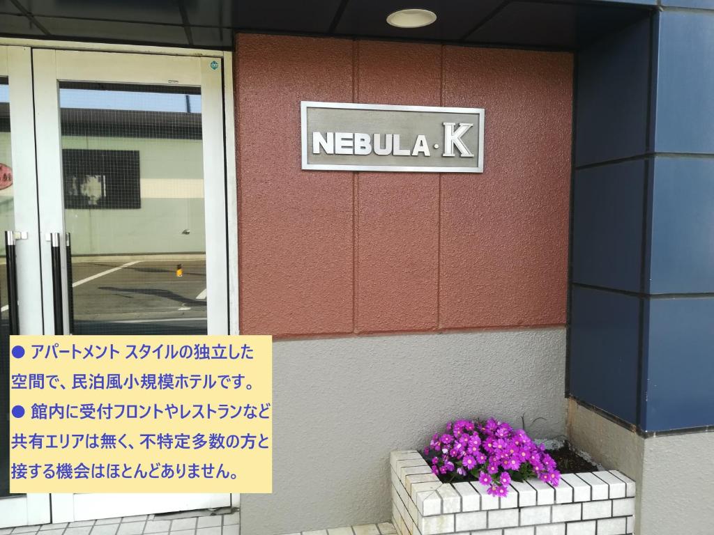 una señal en el lado de un edificio con flores púrpuras en NEBULA K, en Kumagaya