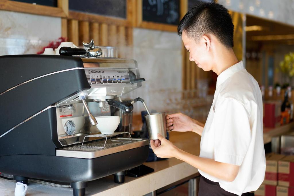 A staff member prepares coffee at a commercial espresso machine beside a hotel service counter.