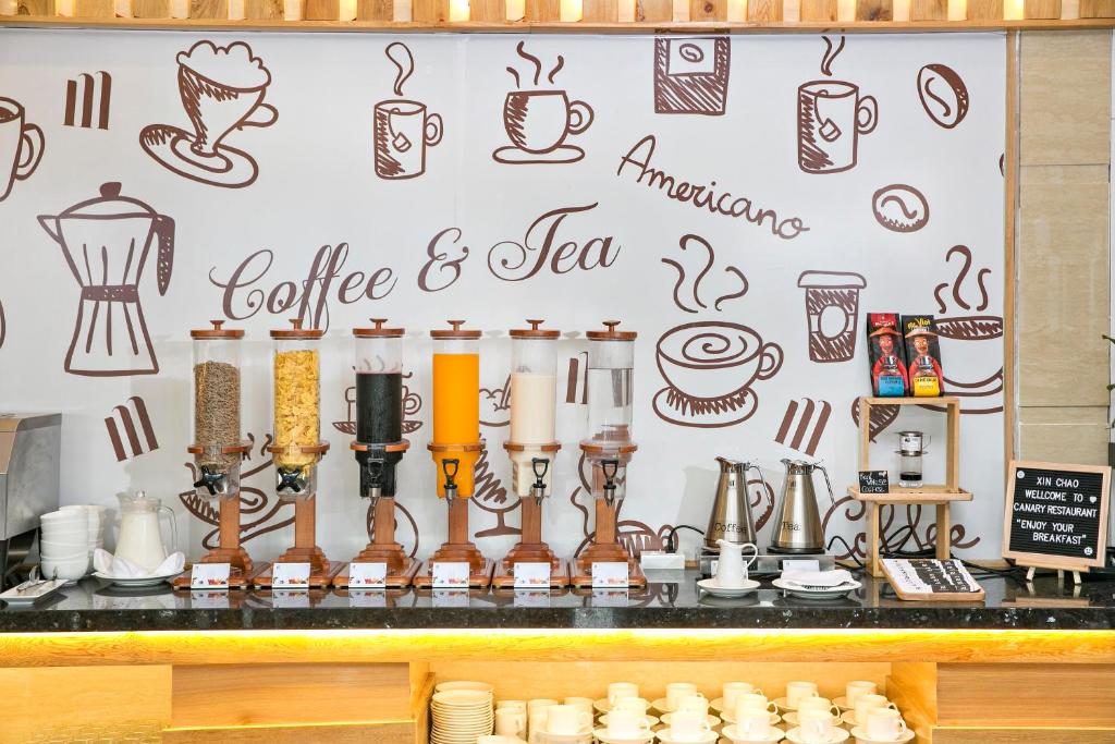 A self-service coffee and tea station with multiple dispensers, cups, kettles, and a decorative drinks wall.