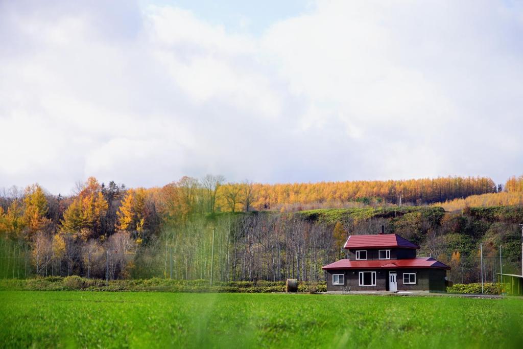 ein Haus mit rotem Dach auf einem grünen Feld in der Unterkunft Farm Stay Ezura Farm in Engaru