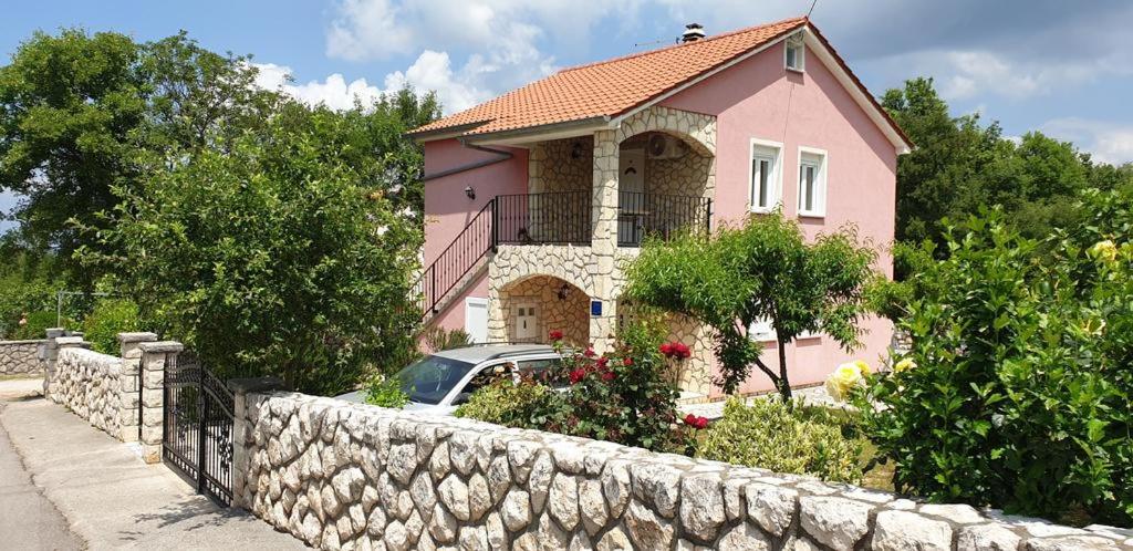 a pink house with a car parked next to a stone wall at Apartments Roses in Dobrinj