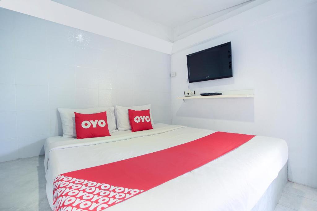 a white bed with red pillows and a flat screen tv at OYO 1054 Phuket Backpacker Hostel in Phuket