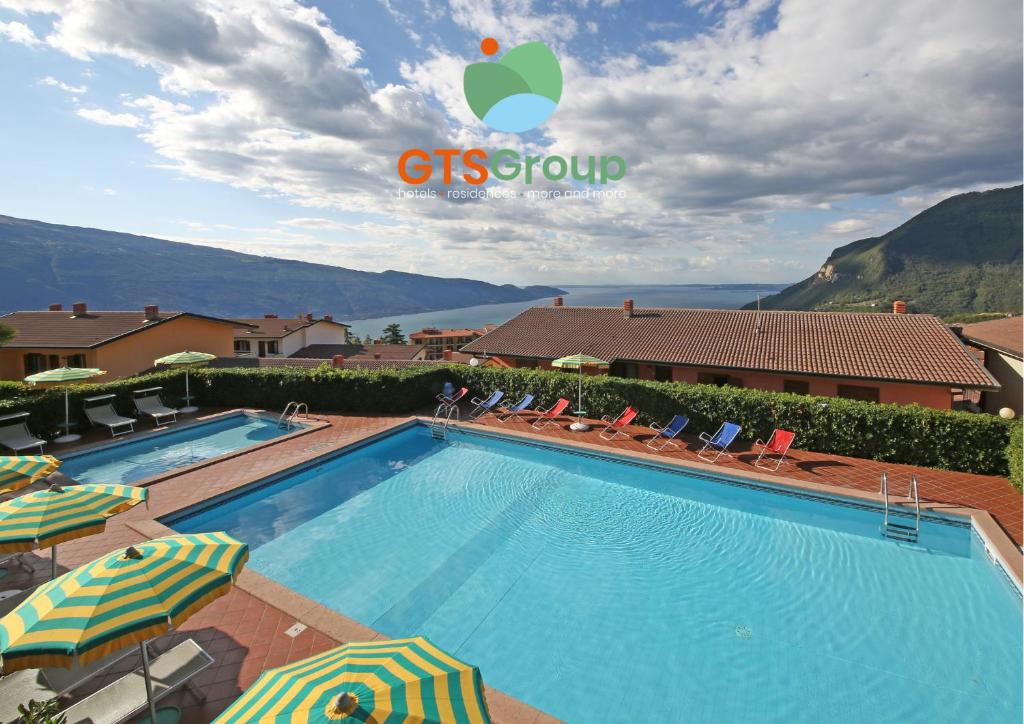 a pool with chairs and umbrellas next to a building at Residence Primera Rompala, GTSGroup in Tignale