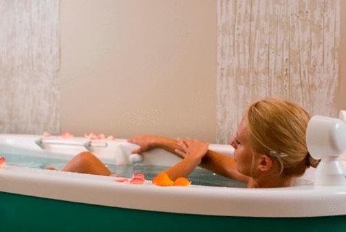 Person relaxing in a bathtub filled with water and flower petals.