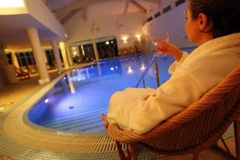 Person relaxing by a pool, holding a drink, in a serene spa setting.