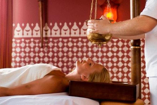 Relaxing spa scene with oil being poured over a woman's forehead.