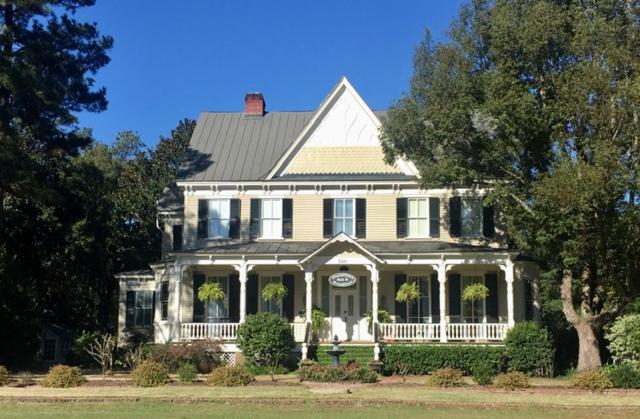 une grande maison blanche avec une terrasse couverte et une horloge. dans l'établissement Flowertown Bed and Breakfast, à Summerville