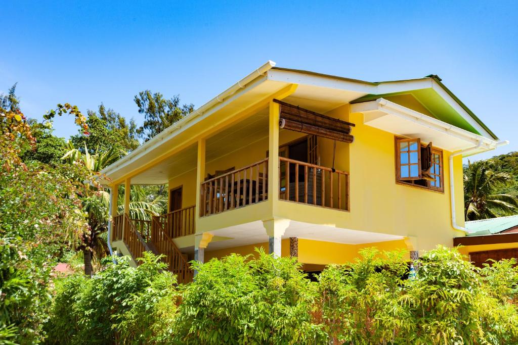 a yellow house with a balcony and trees at Dream Holiday Self Catering in La Digue