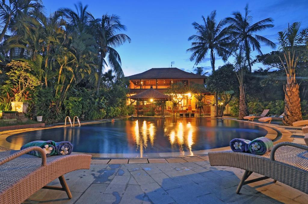 a swimming pool with two chairs in front of a house at Three Brothers Bungalows & Villas in Legian