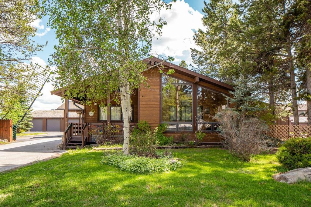 een huis met een veranda rondom en groen gras bij Legacy West in West Yellowstone