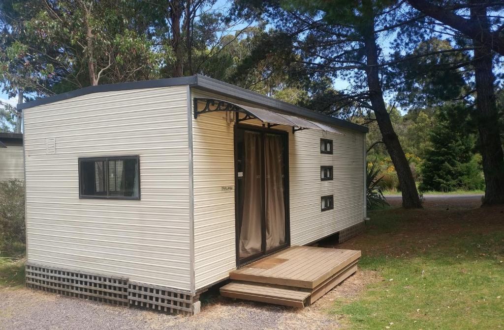 a small white shed with a door and a porch at Zeehan Bush Camp in Zeehan