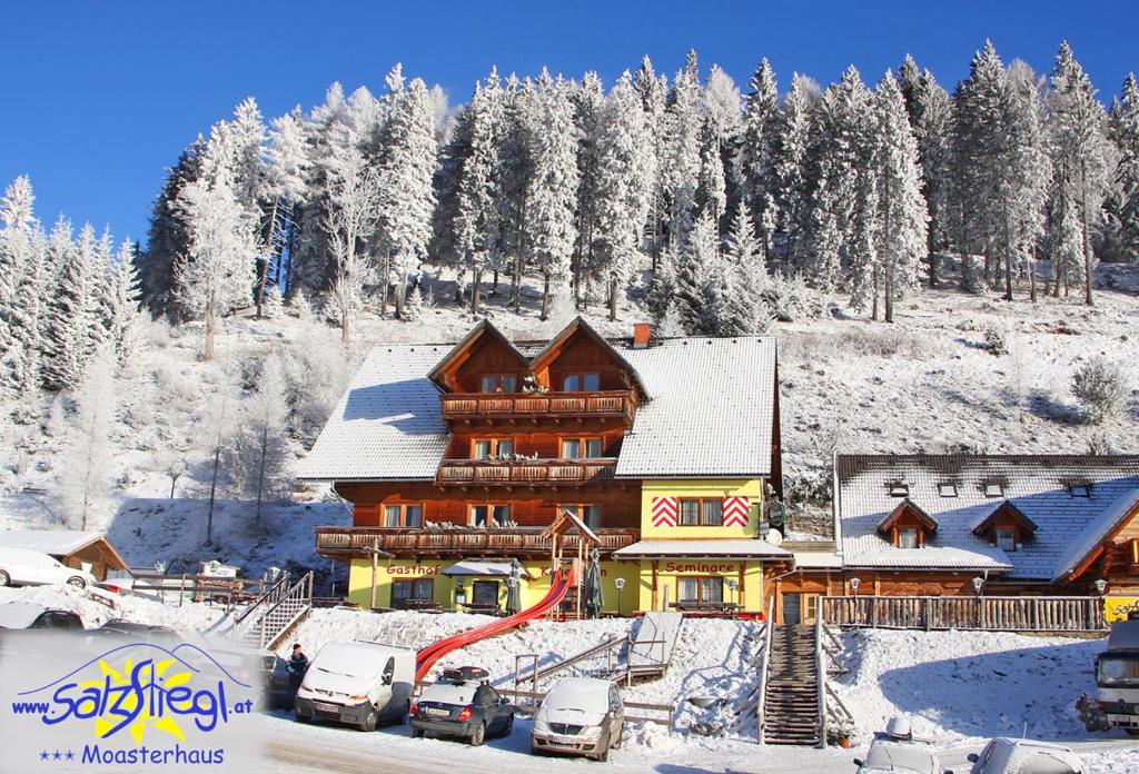 una gran casa de madera en la nieve con coches aparcados en Moasterhaus Trialpark Salzstiegl en Hirschegg Rein