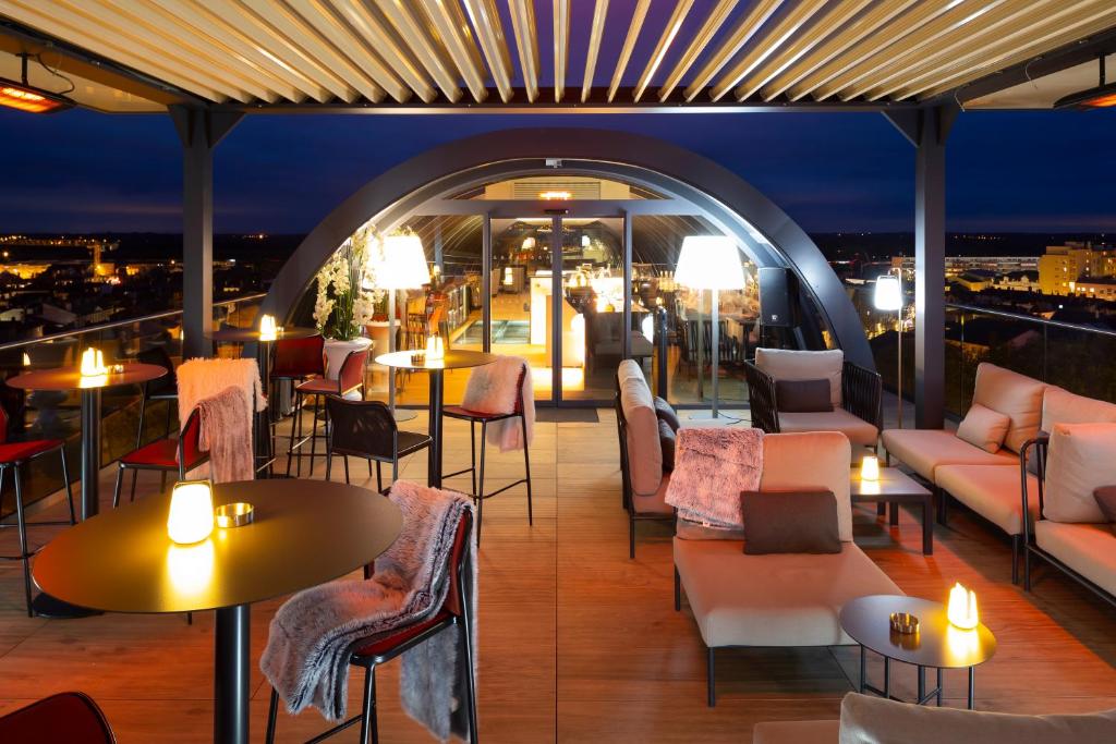 een bar op het dak met tafels, stoelen en verlichting bij HÔTEL & SPA Panorama 360 in Mâcon
