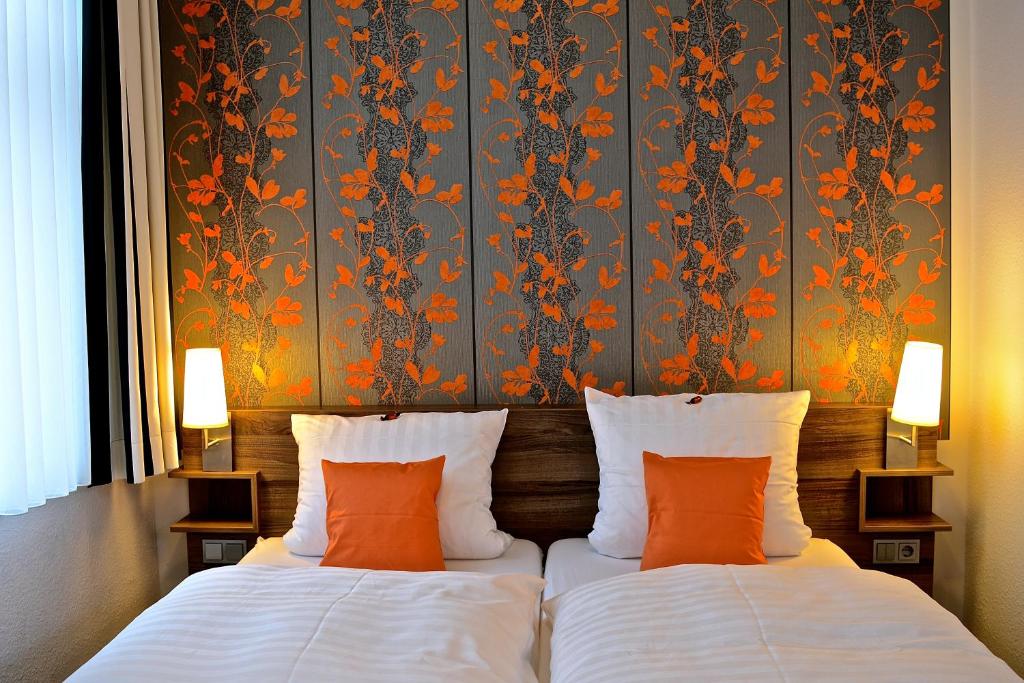 two beds with orange pillows in a hotel room at Hotel Restaurant Telgter Hof in Telgte