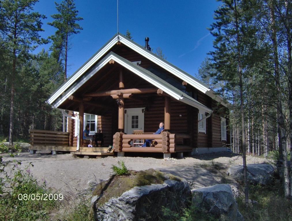 a cabin in the woods with a person sitting on the porch at KoliCarelia Cottages in Hattusaari