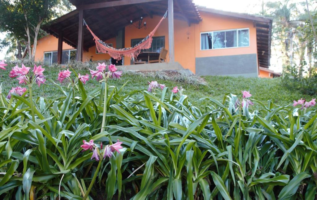Chalé Bosque Do Barreiro في أراكسا: حديقة بها زهور وردية أمام المنزل