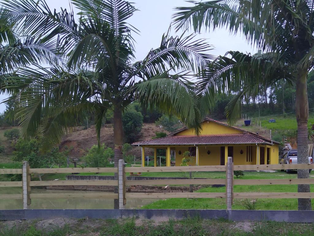 a yellow house with a fence and palm trees at Sítio Elias in Lauro Müller